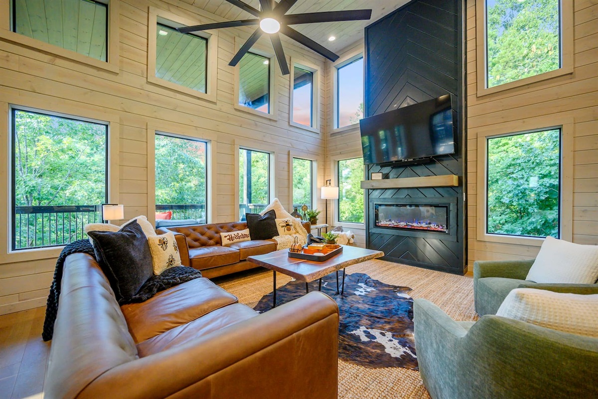 Living room features vaulted ceilings, 2 plush leather couches, 2 swivel chairs, and lots of pillows and throw blankets to snuggle up with for a movie night on the 65" TV above the linear fireplace.