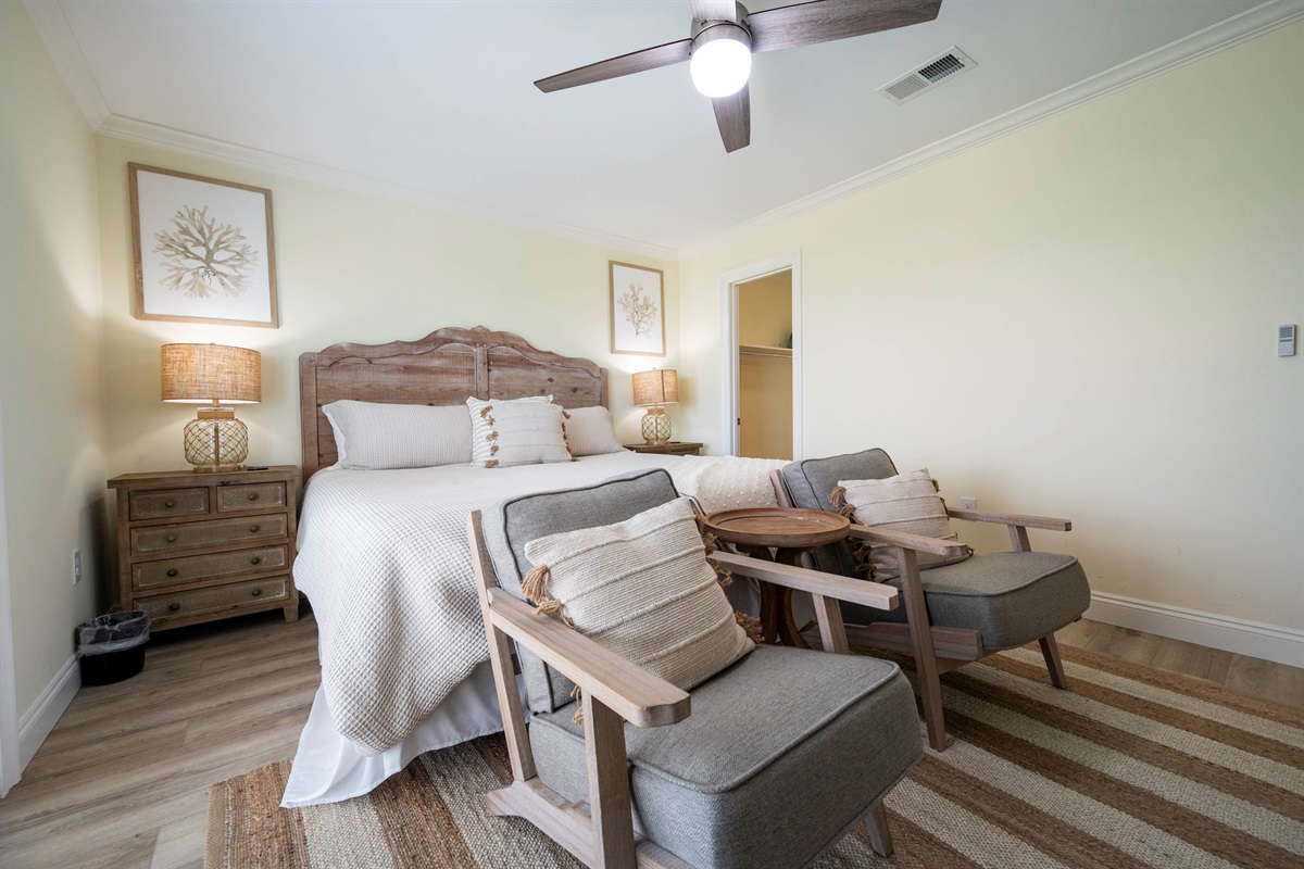 Charming bedroom retreat with rustic decor, soft neutral tones, and cozy seating- opening to a balcony with peaceful views of Little Lagoon.
