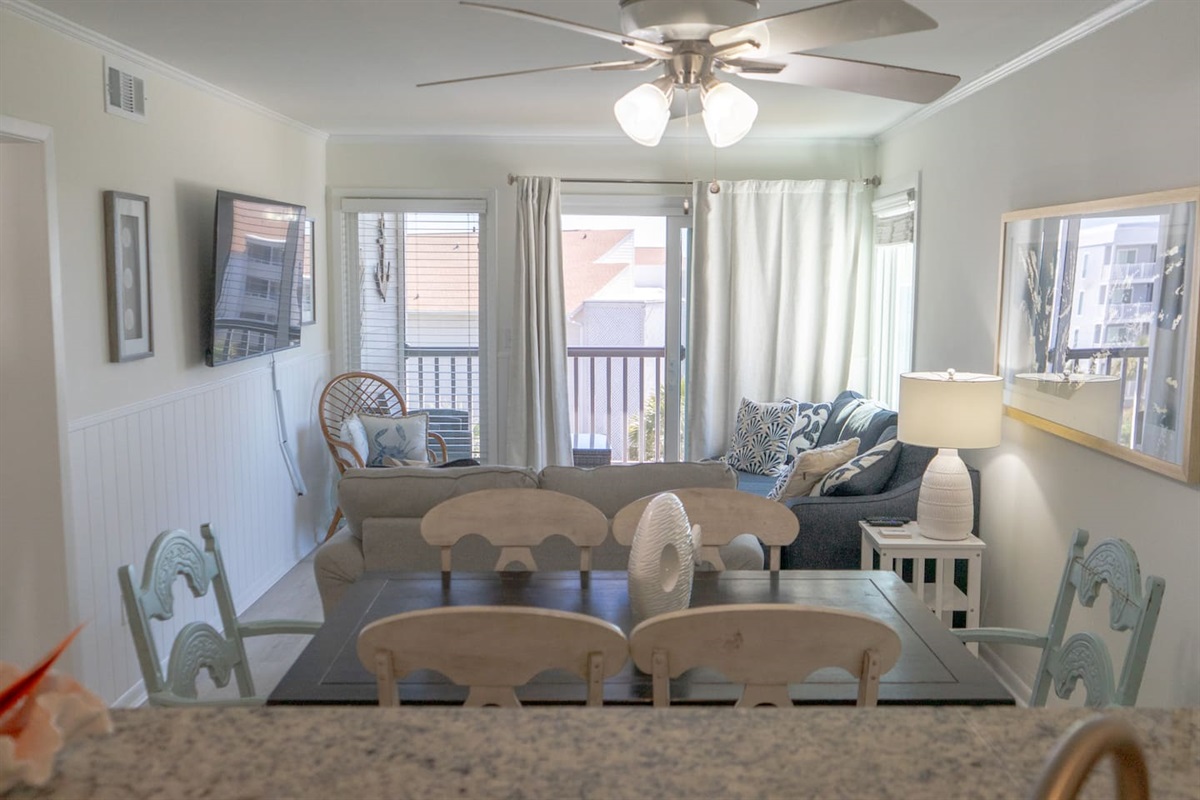 Open living and dining space features cozy seating, beach-inspired décor, and plenty of natural light pouring in from the balcony doors