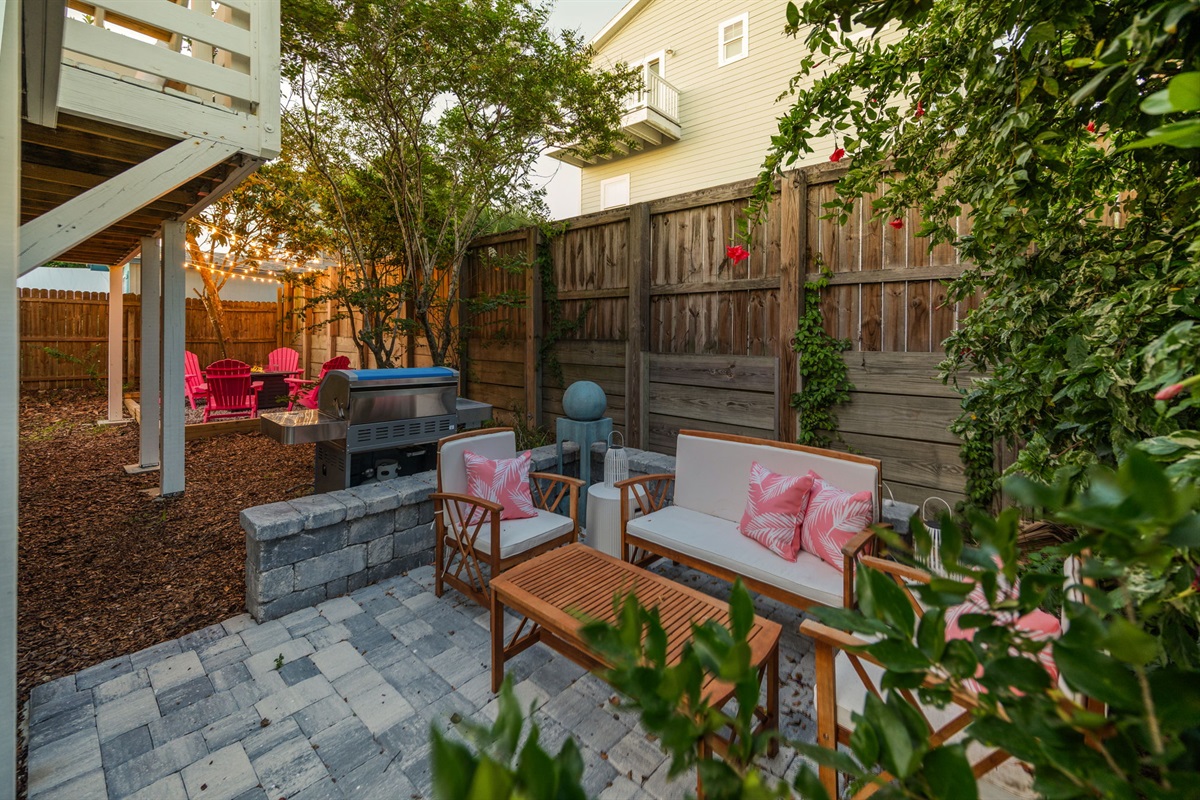 Here’s a view of the cozy, tropical backyard—lush and inviting with a grill, firepit, and patio area. You’ll even spot a lime tree, adding a fresh touch to this serene outdoor space!