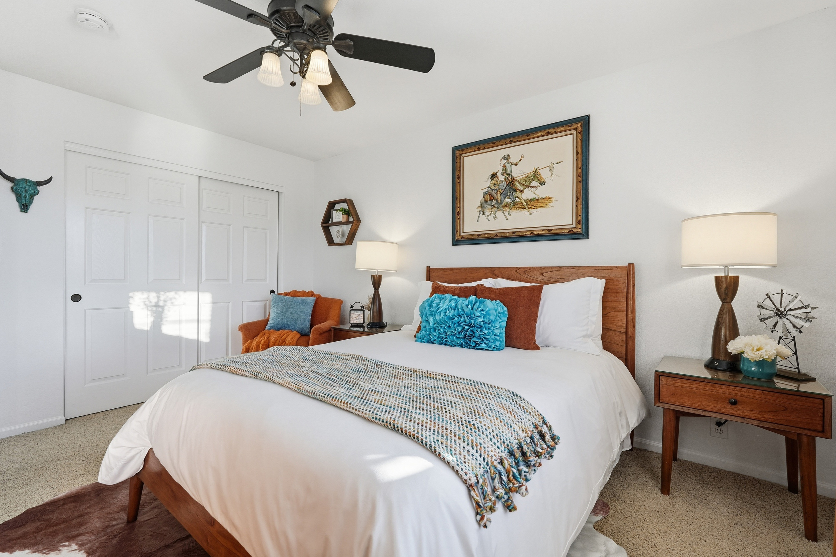 Queen bedroom with accent chair, ceiling fan, bedside lighting, and warm styling for a comfortable stay.