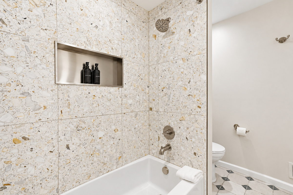 Spa-like bathroom with stone tile, built-in niche, polished chrome fixtures, and a deep soaking tub. Bright, modern design with clean lines and a calm, upscale, hotel-inspired feel.