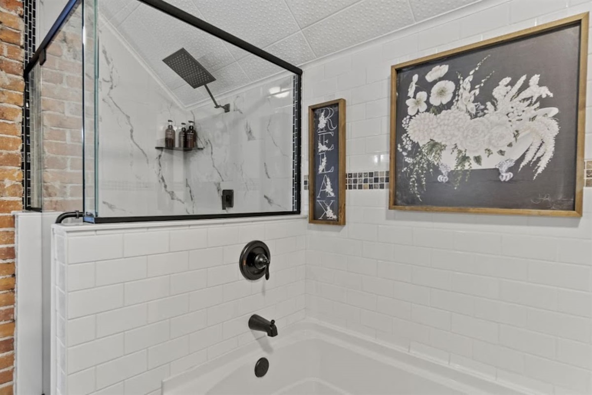 Luxurious full bathroom showcasing a glass-covered shower, a sleek bathtub, modern lighting, stylish picture frames, elegant tiles, and beautifully designed walling—offering a perfect blend of comfort, functionality, and sophistication