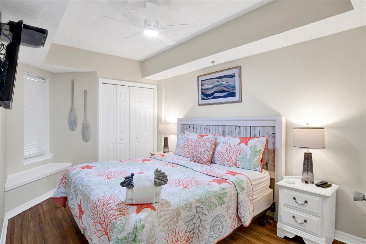 Primary bedroom with king bed, wall mounted smart TV, ceiling fan and en-suite bathroom 