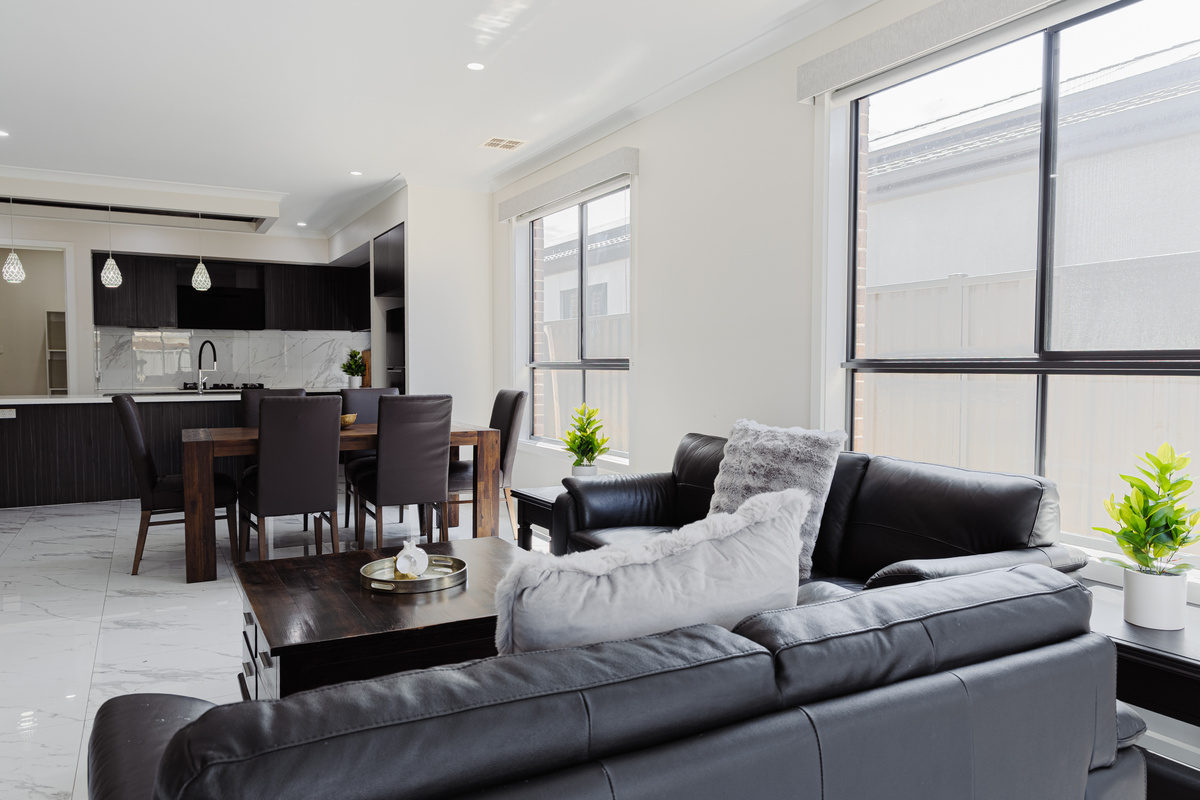 Bright open-plan living and dining area with lounge seating, large windows and tiled floors.