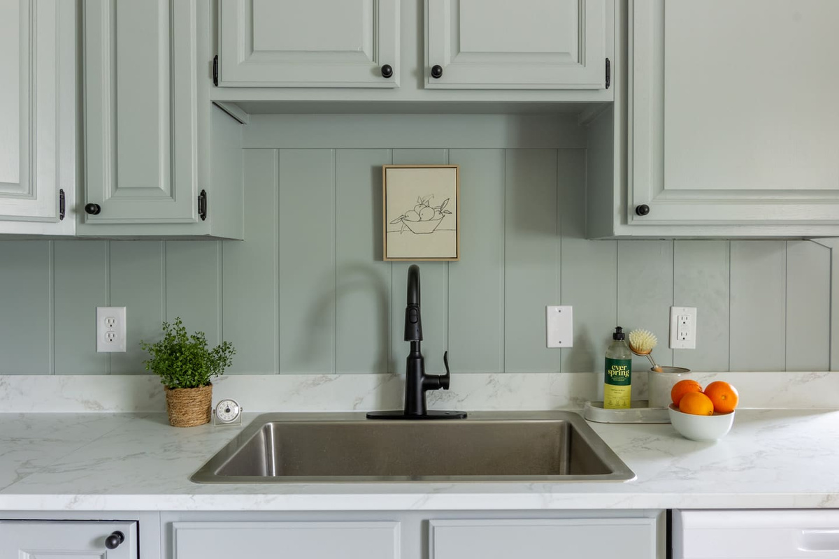 Sage cabinetry and a marble-look counter give the sink area a fresh, cheerful feel.