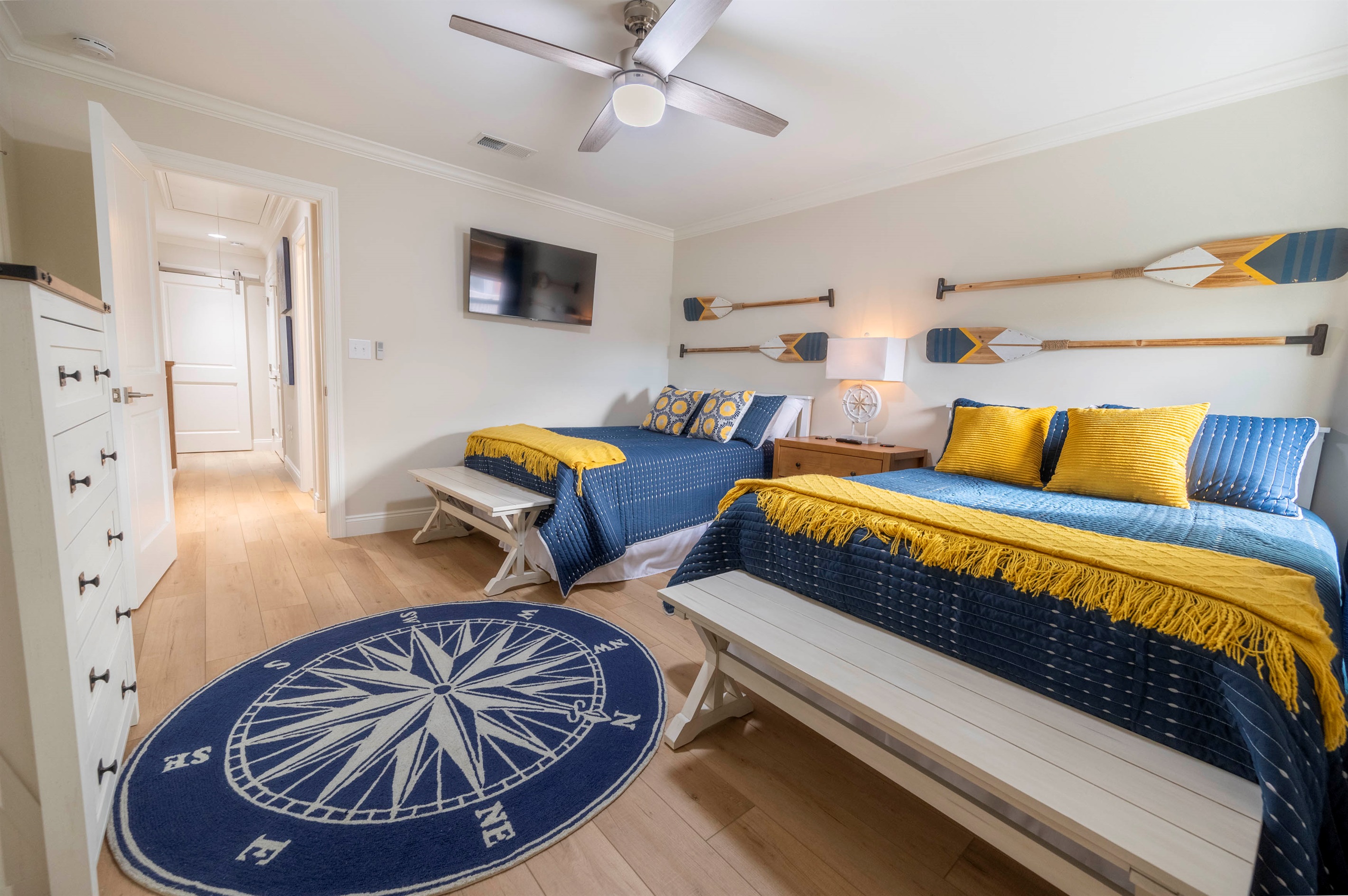 A charming, seaside-inspired retreat, this cozy twin bedroom features a cheerful navy and yellow color palette, accented by rustic oar wall decor and a thematic compass rug, creating a perfectly styled maritime getaway