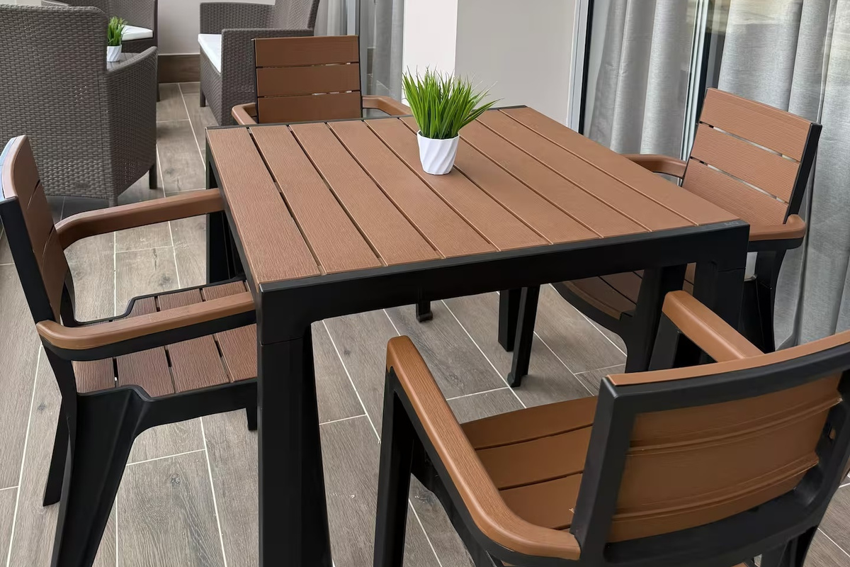 Zona de comedor cubierta en el balcón con mesa y asientos, suelo de baldosas y una zona lounge cercana para disfrutar de momentos relajados entre el interior y el exterior.