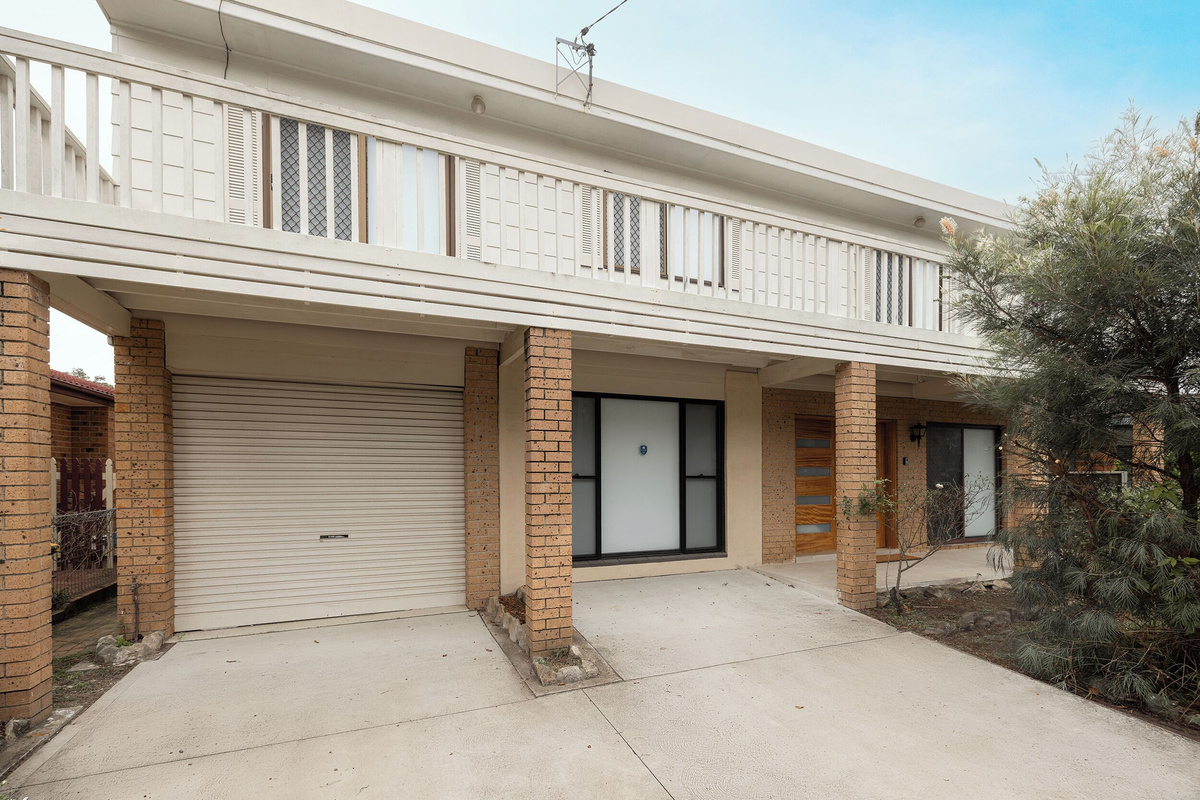 The front exterior at Luna’s Sanctuary shows the garage, driveway, covered entry and full-width balcony across the upper level.