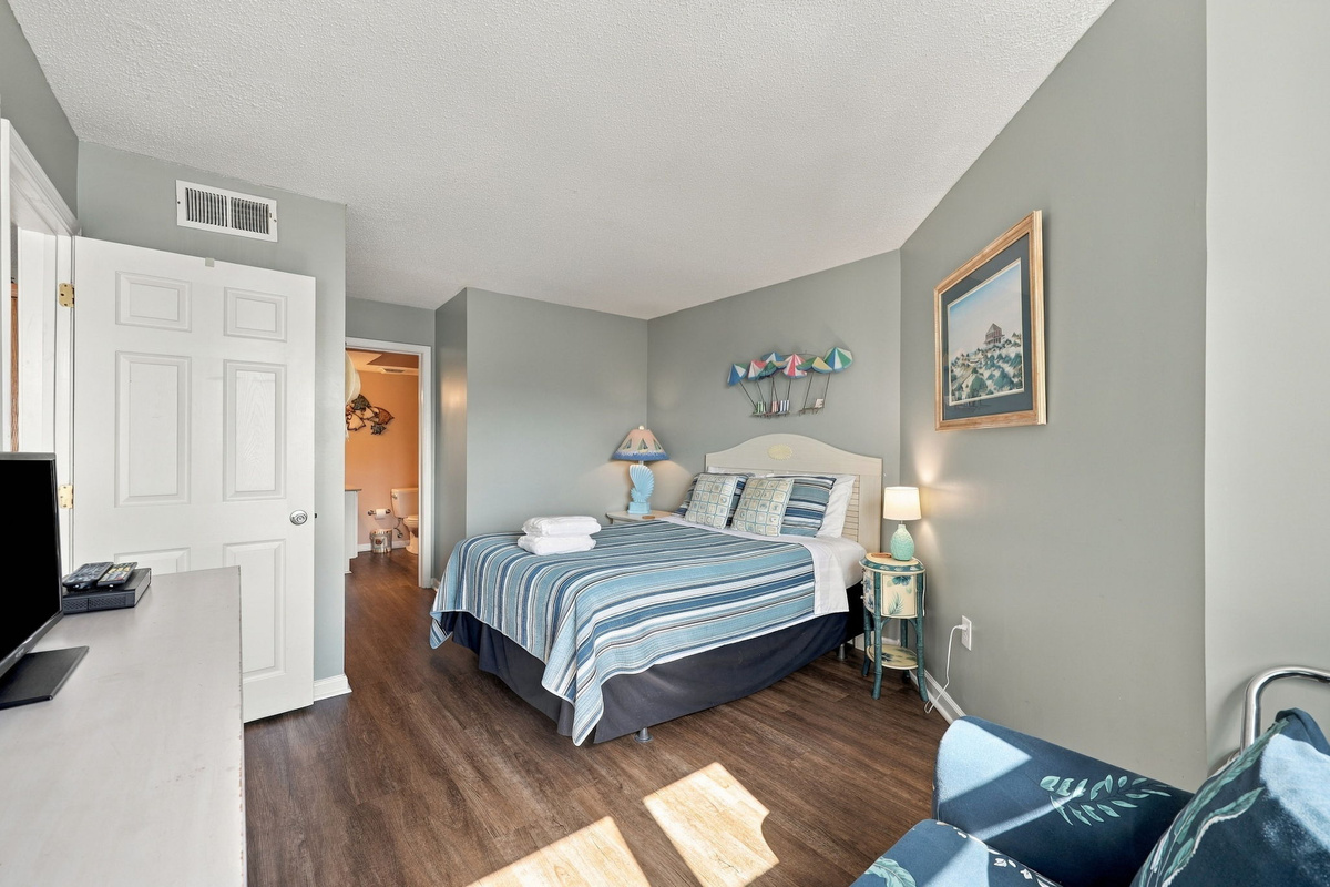 Inviting master bedroom featuring a queen bed with blue striped bedding, light blue walls, and direct hallway access.