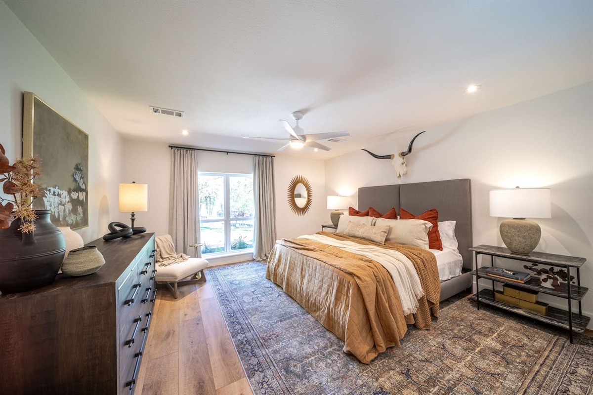 Spacious primary bedroom with king bed, layered neutral bedding, warm accents, and thoughtful lighting. Includes a TV, a well-sized walk-in closet, and a private ensuite for comfort and convenience.