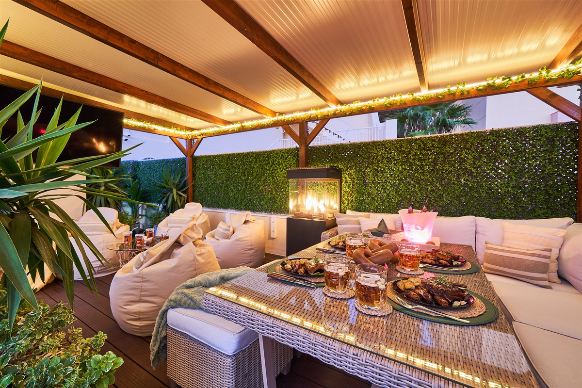 Relax beneath the covered pergola with cozy seating, fireplace, and dining area. Perfect for long evenings, romantic dinners, or movie nights on the outdoor TV under soft ambient lights.