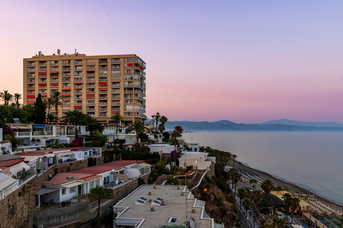 Evening coastline view with the beach, palms and distant mountains.