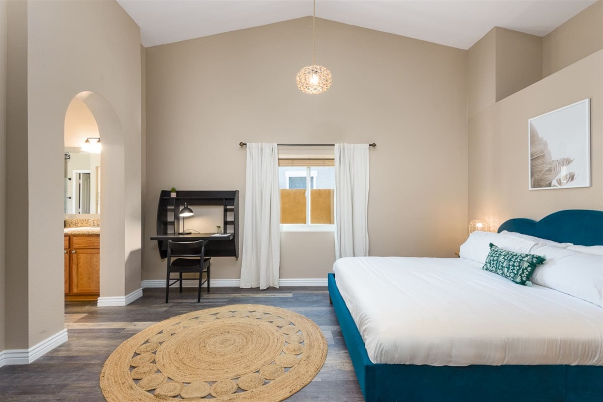 Primary ensuite bedroom with a spacious bed, dedicated workspace, high ceilings, and a bright, open layout for a comfortable stay.