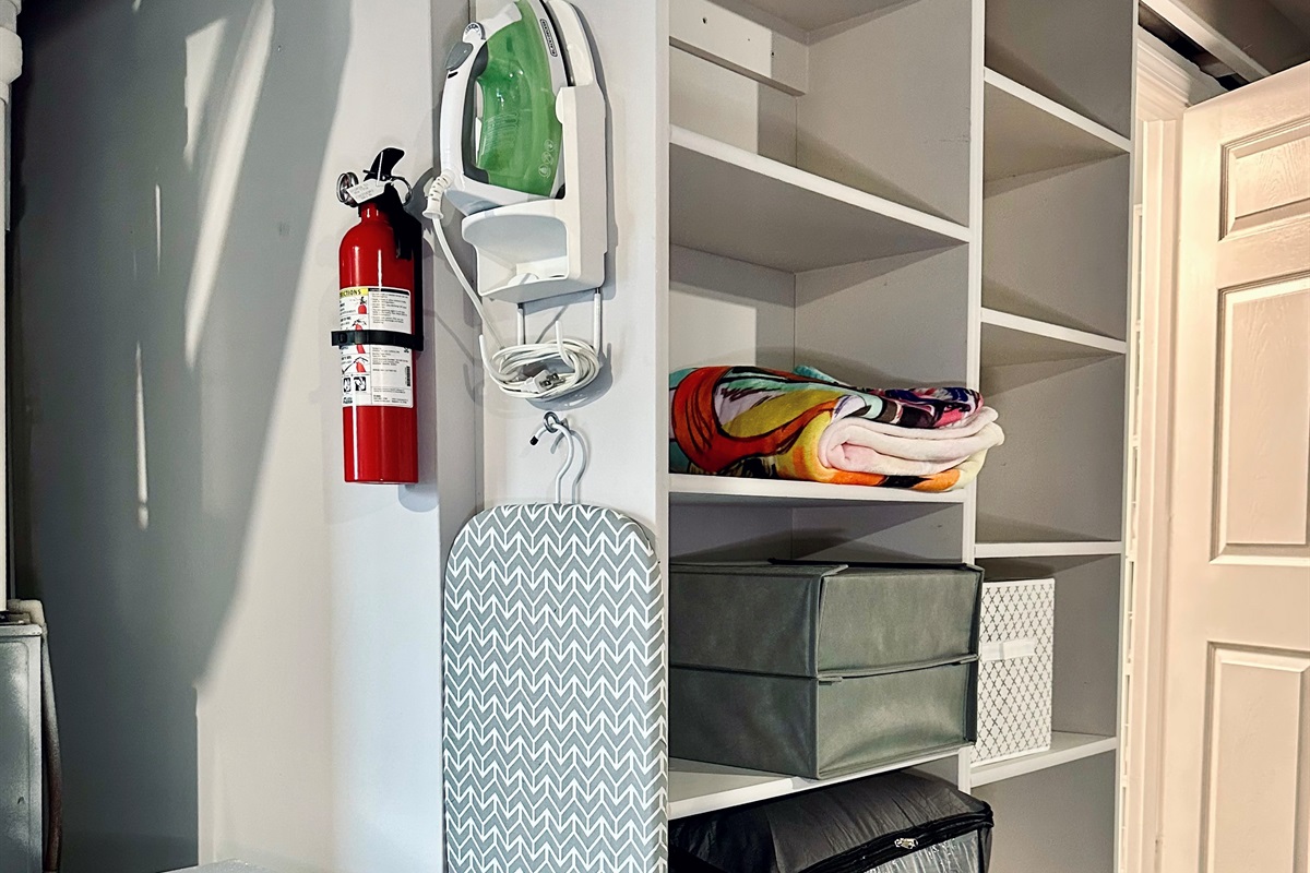 Ironing station with mounted iron and board, plus open shelving just outside the basement bathroom. Includes extra bedding and linens for the lower-level sofa bed and convenient storage space for guests