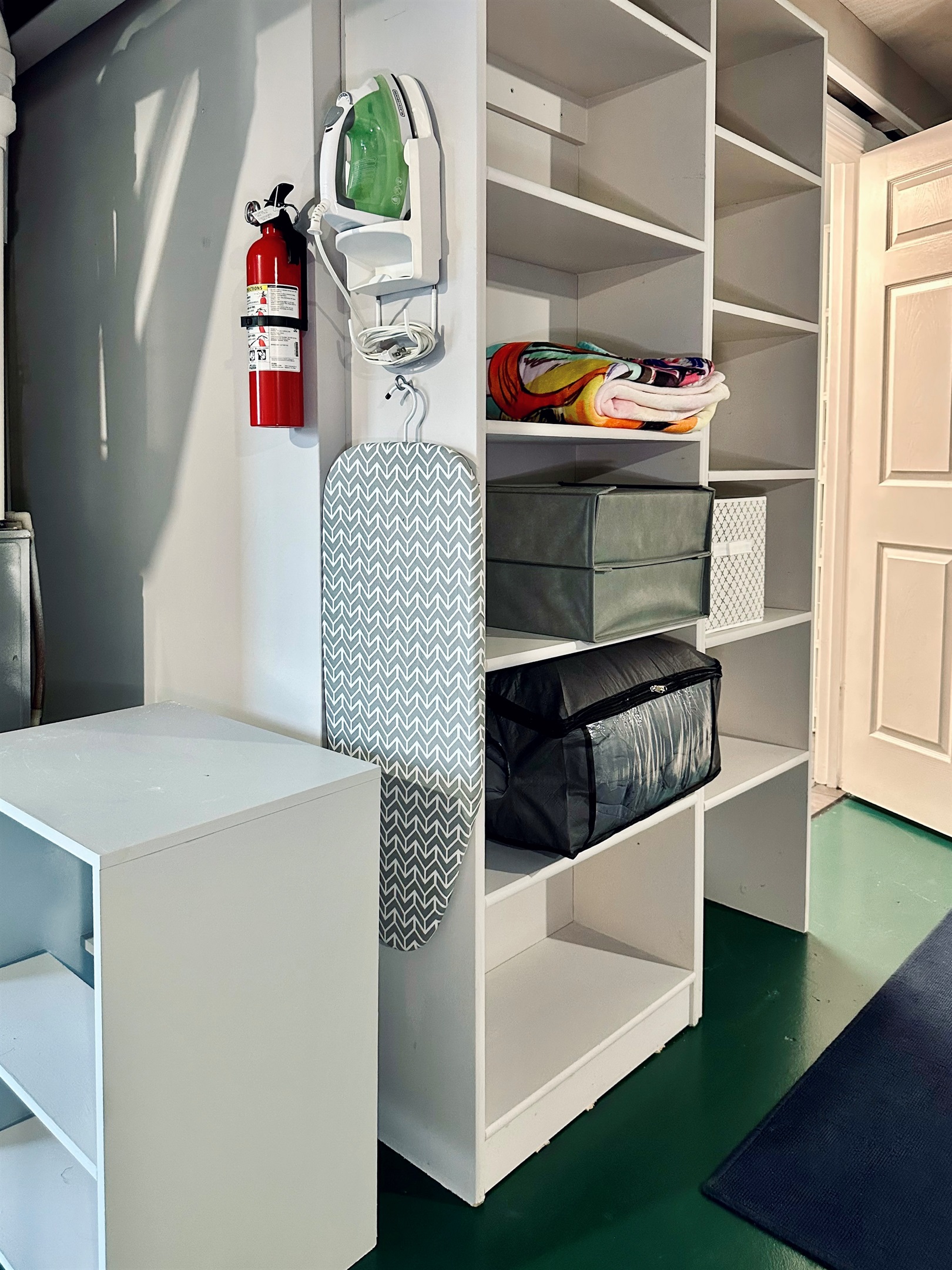 Ironing station with mounted iron and board, plus open shelving just outside the basement bathroom. Includes extra bedding and linens for the lower-level sofa bed and convenient storage space for guests