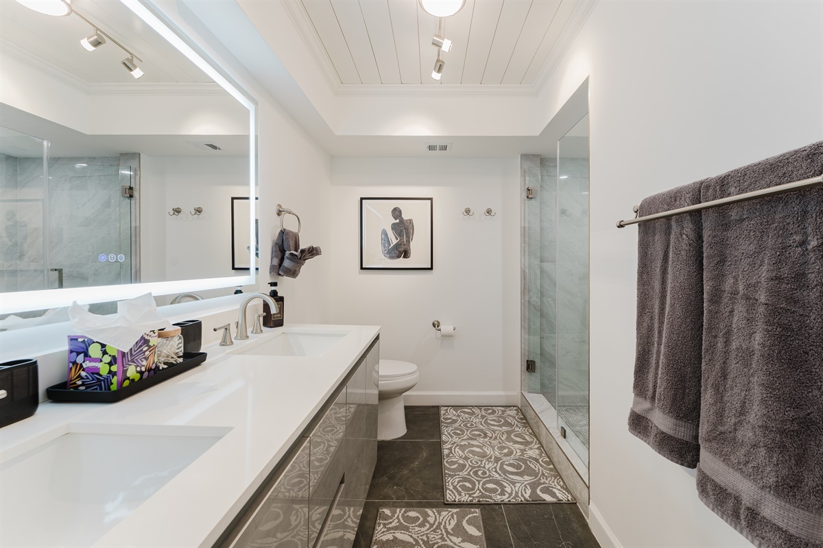Spacious primary bathroom with double vanity, LED-lit mirror, and modern walk-in glass shower.