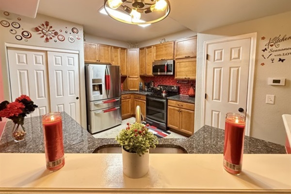 This kitchen showcases warm wood cabinets, dark granite counters, and a bold red tile backsplash with stainless steel appliances. Decorative elements and plants add charm and warmth to the spa