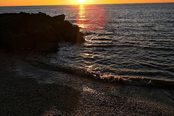Witness stunning waterfront sunsets. The sun dips below the horizon, reflecting brilliant orange light across the rippling waves and rocky jetty for a truly magical evening view.