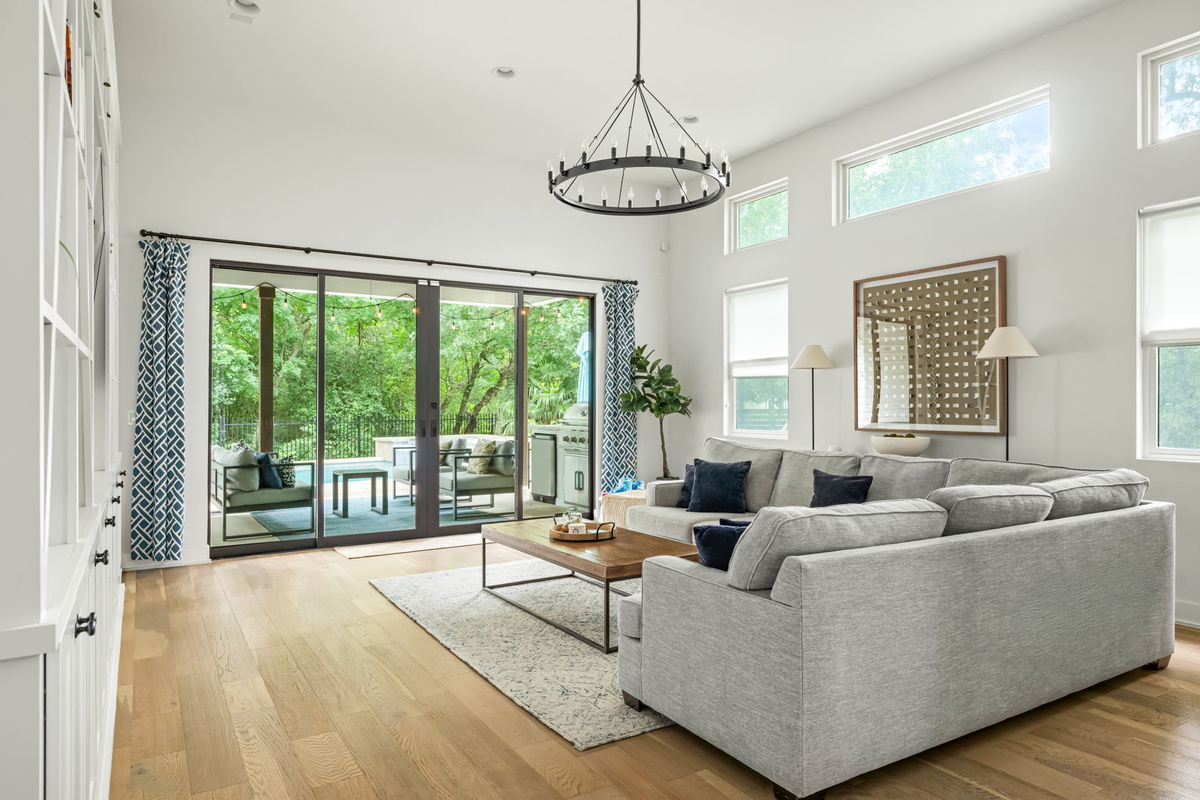 Sun-drenched living room with soaring ceilings, floor-to-ceiling sliding glass doors, and serene backyard views — bringing the outdoors in.