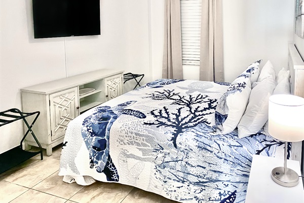 Bedroom with king bed, wall mounted TV, ceiling fan, dresser and ensuite bathroom