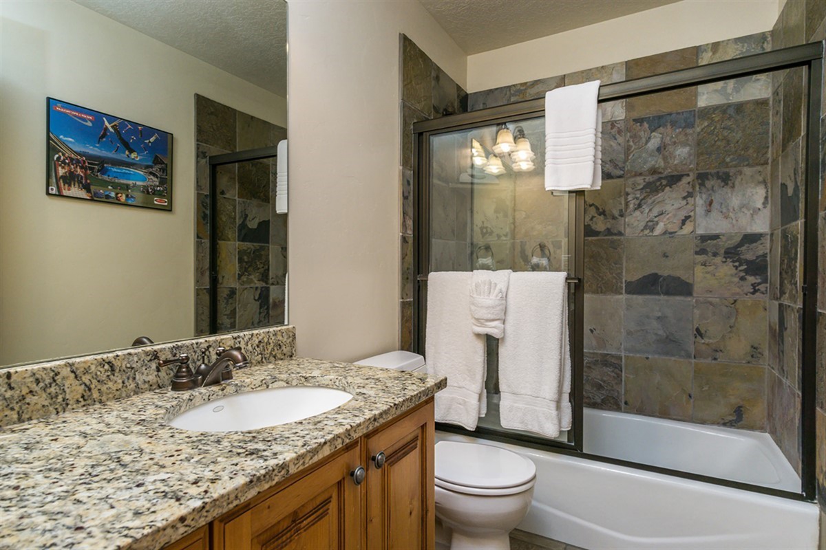 A beautifully finished bathroom with granite countertops and a tiled shower, blending modern convenience with mountain elegance.