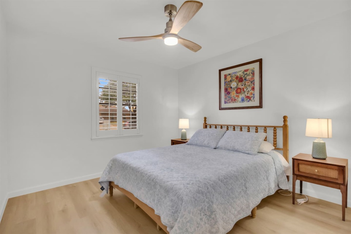Inviting queen bedroom with a queen bed, warm lighting, room darkening shades, and a modern ceiling fan. Relax in a calm, airy setting with plenty of natural light.
