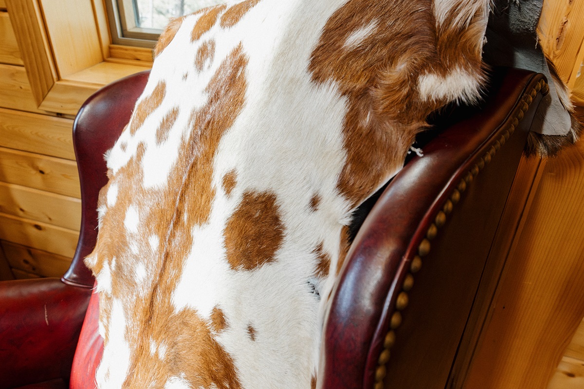 Cozy cabin corner with a plush leather chair, layered textures, and forest views—perfect for reading, morning coffee, or unwinding after a day of hiking in this warm, rustic White Mountains A-frame cabin.