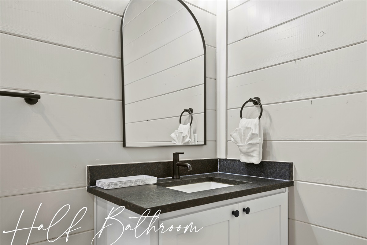 The Half Bathroom offers a quaint and convenient space to refresh, featuring a sleek vanity set against the classic shiplap backdrop.