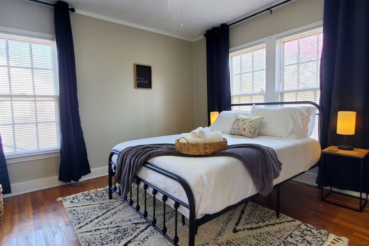 Bright and serene bedroom featuring a cozy queen bed with crisp white linens, soft lighting, and a decorative floral pillow—perfect for a restful stay.