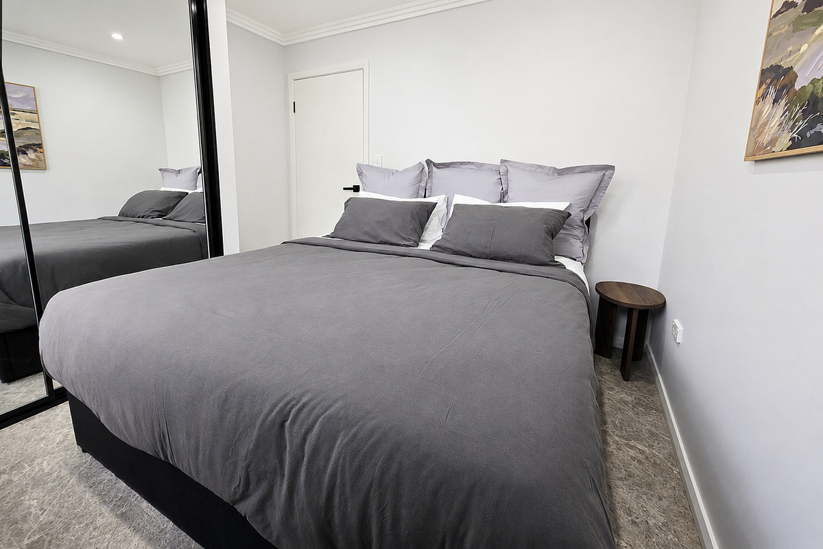 The side table sits beside the bed, with the mirrored wardrobe positioned along the opposite wall for easy access.