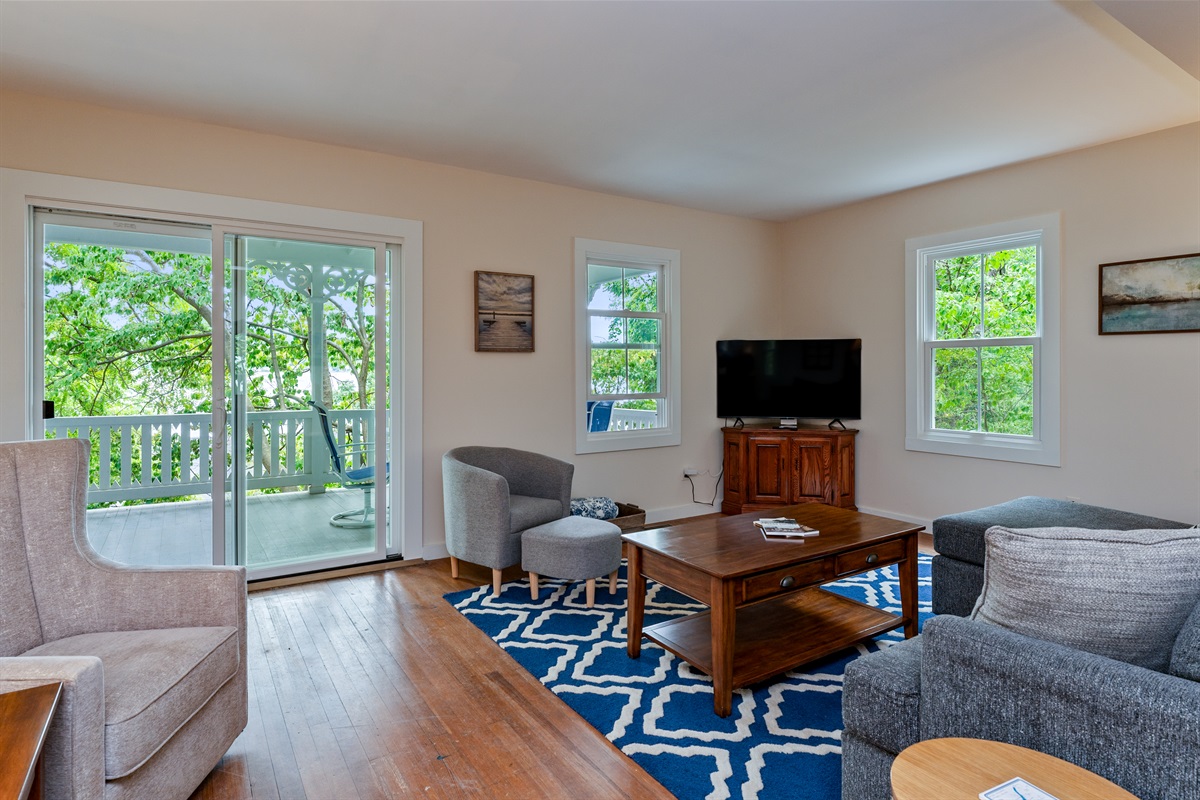 Relax in a bright living room with a large sliding door opening to the porch, surrounded by lush greenery and peaceful lake views.