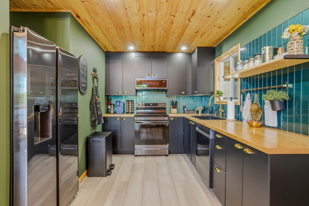 Kitchen with stainless appliances, teal backsplash, butcher block countertops, and open shelving
