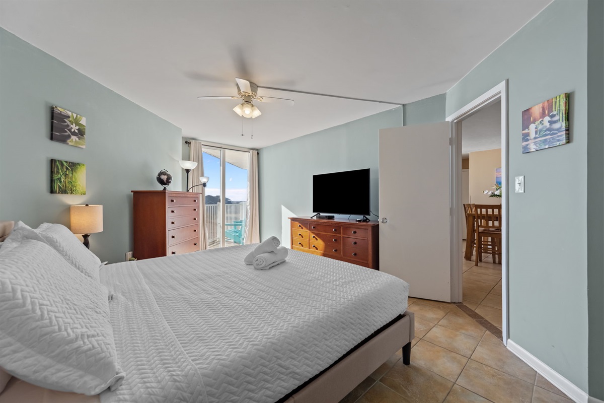 Spacious Master bedroom with a comfortable King bed, dresser, TV, and sliding doors opening to a private balcony