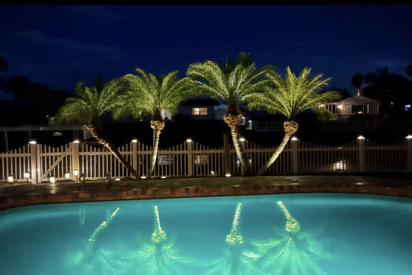 Illuminated pool and tropical waterfront setting after sunset.