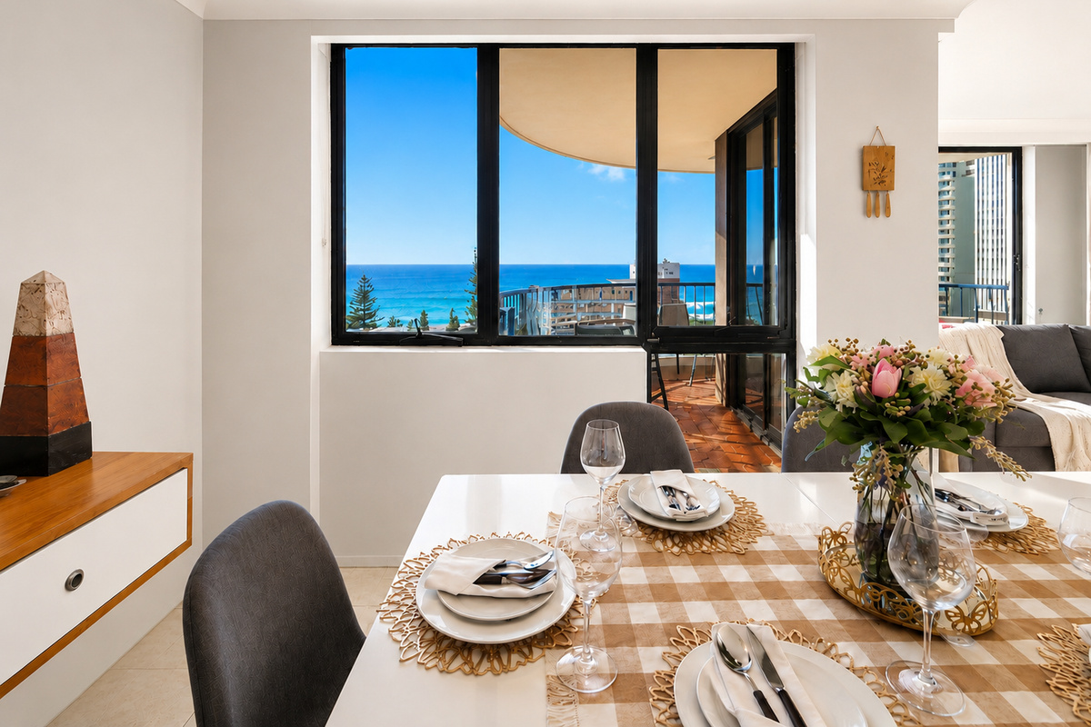 Ocean blue fills the view beyond the dining table at Robin’s Oceanview Penthouse, giving the open-plan living zone a strong coastal connection.