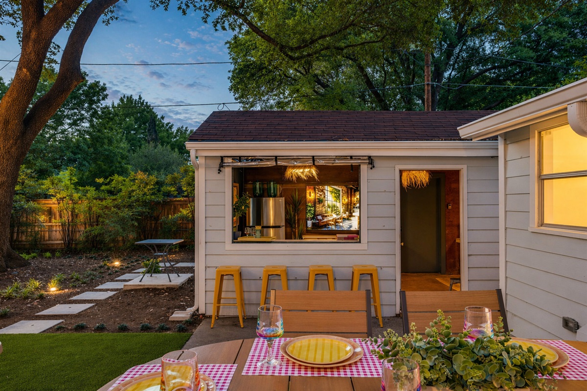 Backyard entertaining done right. A pass-through bar window opens to the patio where string lights, a styled dining table, and mature shade trees set the scene for effortless indoor-outdoor living in Westworth Village.