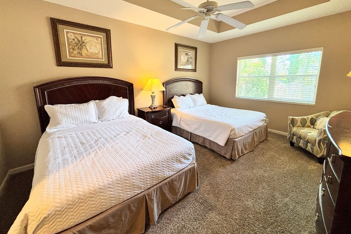 Spacious bedroom featuring two comfortable beds, tray ceiling with ceiling fan, cozy seating area, and plenty of natural light.