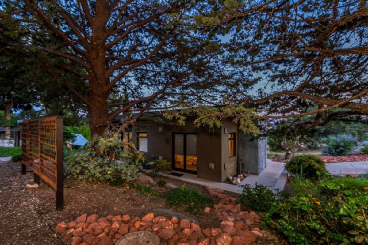 Secluded evening view nestled beneath mature trees, offering a tranquil setting with warm interior lighting glowing through the windows.