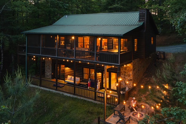 🔥 Nightfall at Cooper’s Ridge. Multi-level outdoor living with mountain views. Guests can enjoy panoramic scenery from the private hot tub, screened-in porch, or while gathered around the fire pit with string lights.