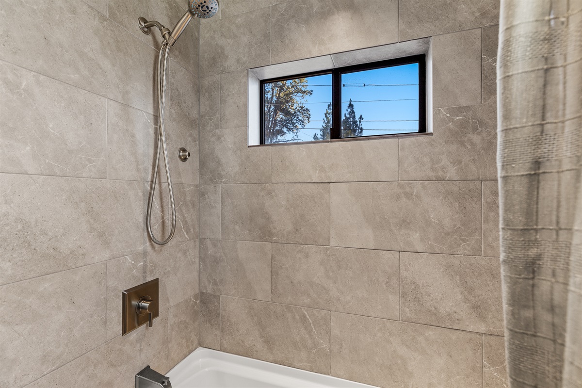 Bright guesthouse tub/shower with modern tile, natural light, and a refreshing shower experience.