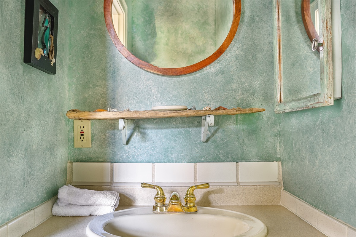 The convenient main floor half-bath features unique coastal textures and a custom driftwood shelf. This thoughtfully designed powder room ensures comfort and accessibility for your group without needing to head upstairs during the day.