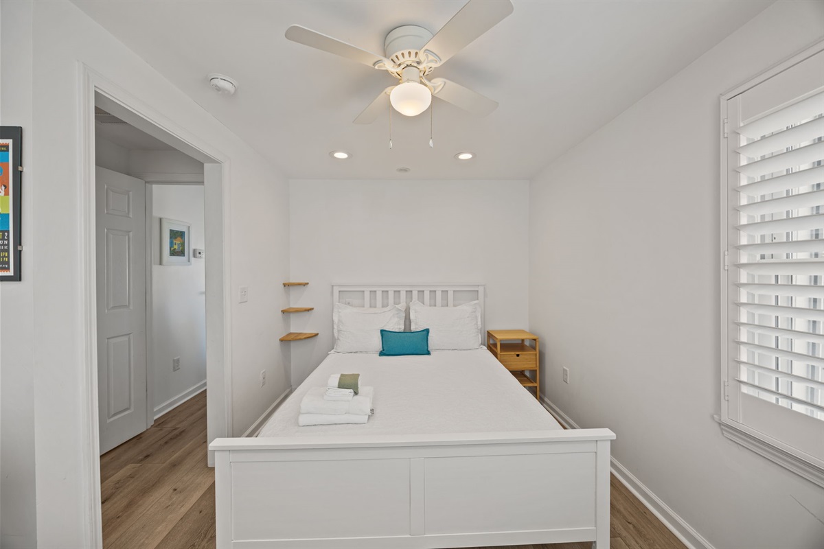Bright master bedroom retreat with a queen bed, ceiling fan, and calm coastal style