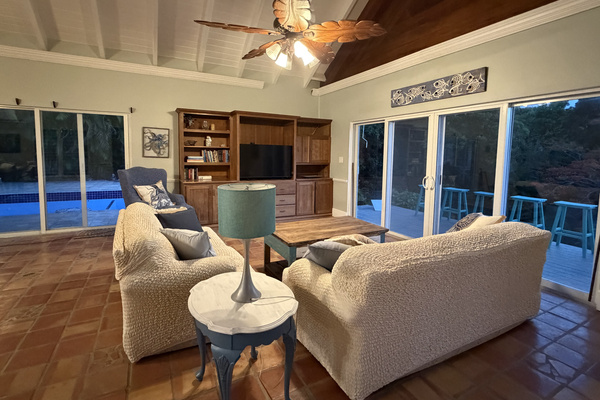 Sliding glass doors surround the room, flooding the space with natural light and opening directly to a private pool deck on one side and a deck with outdoor seating on the other—bringing seamless indoor-outdoor living right to your fingertips.