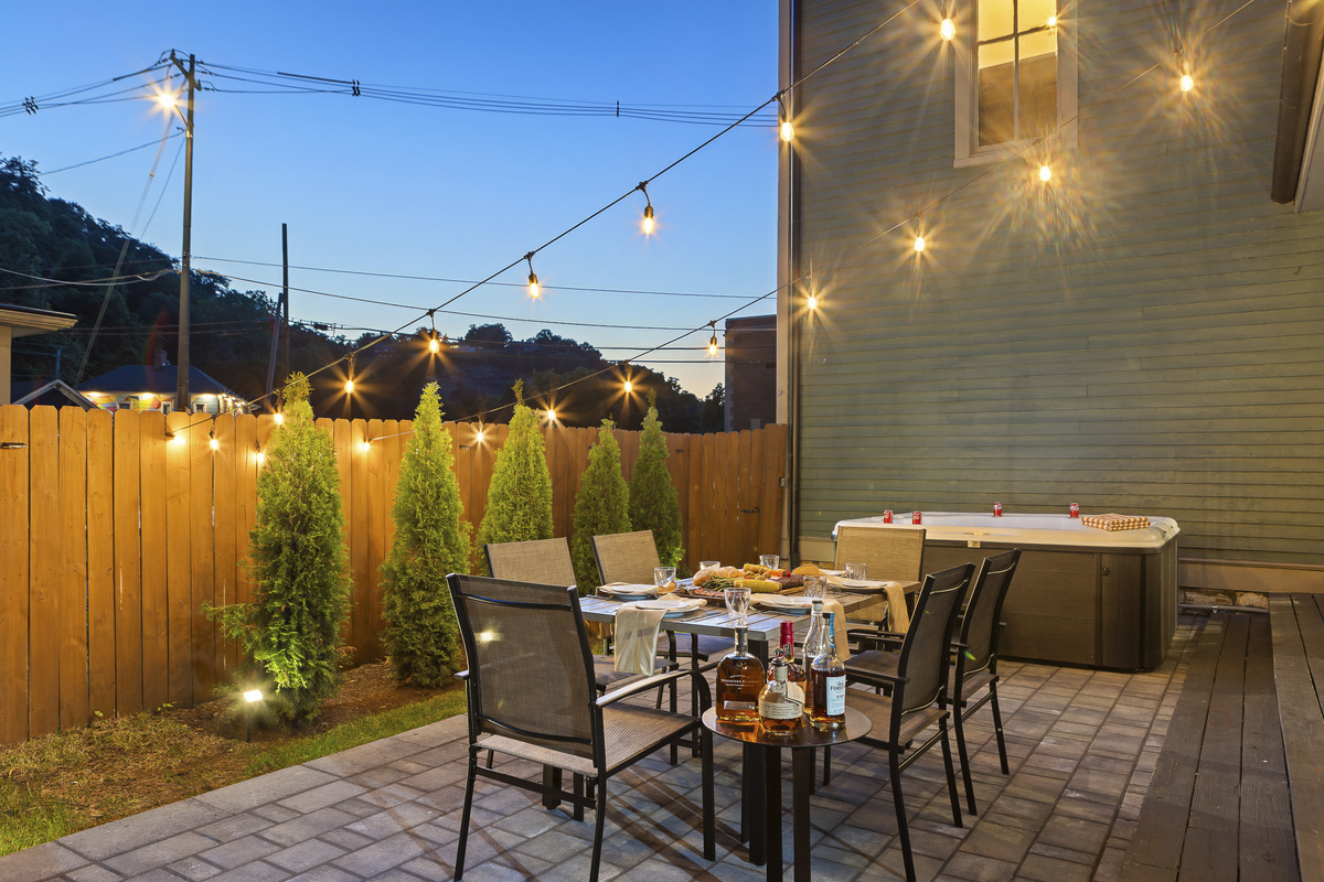 As the sun dips low, the string lights come to life, with bourbon on the table and the hot tub glowing nearby.