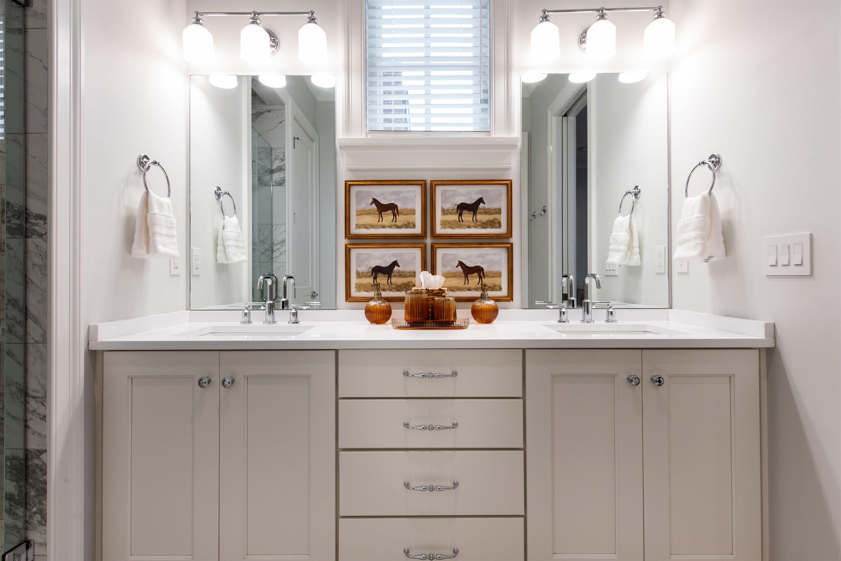njoy the luxury of space with this beautifully appointed bathroom, featuring dual sinks, ample storage, and elegant decor with horse-themed artwork. Perfect for your stay on the Bourbon Trail, combining comfort with a touch of Kentucky's equestrian charm.