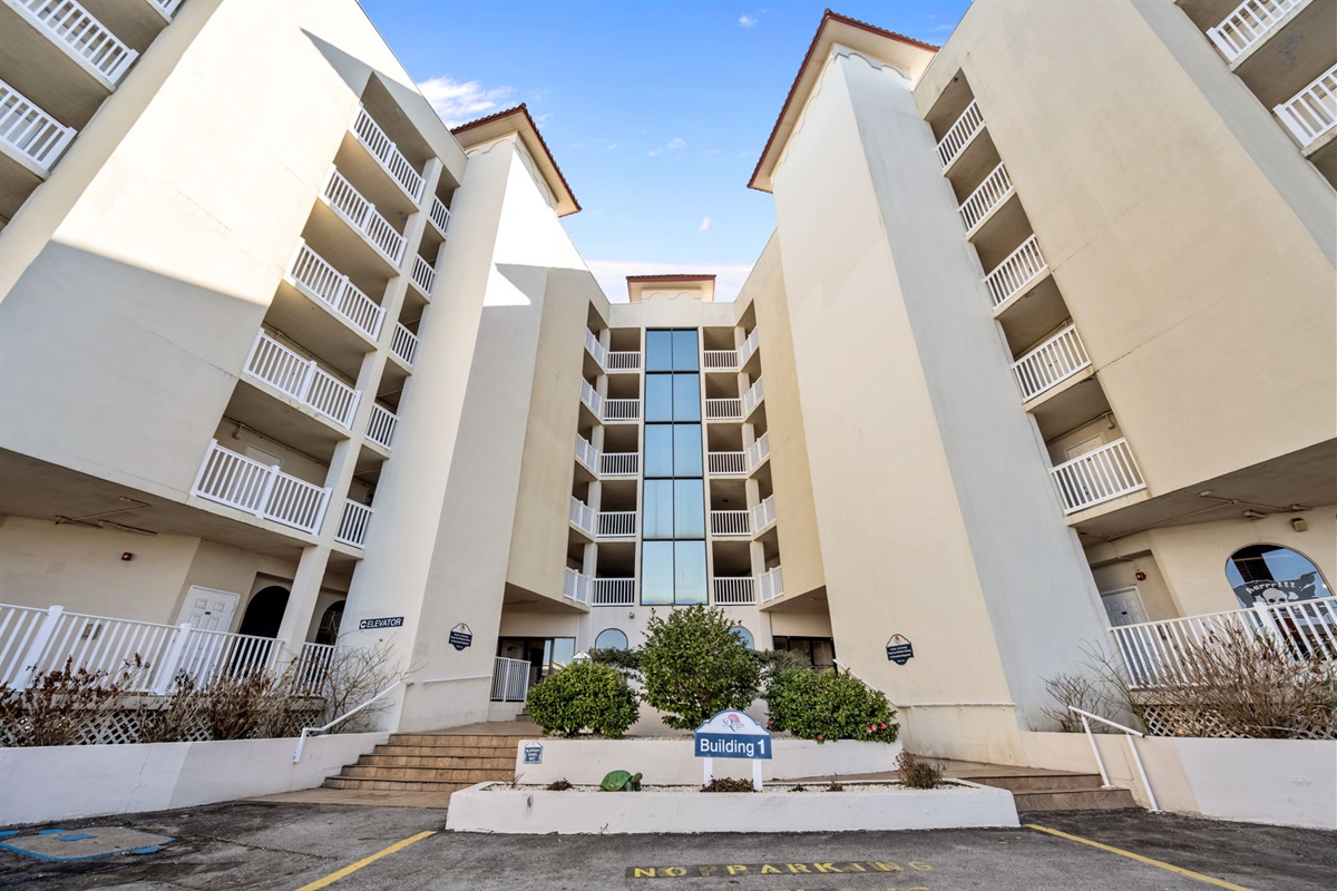 Grand front view of building 1, featuring a central glass elevator tower, and a clearly marked entrance for easy check-in and access to your stay at "Dolphin Sightings"