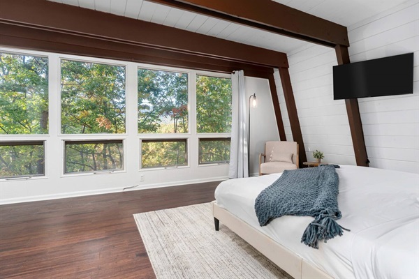 Full wall of windows in master bedroom offers views of trees and mountain ridge in background.