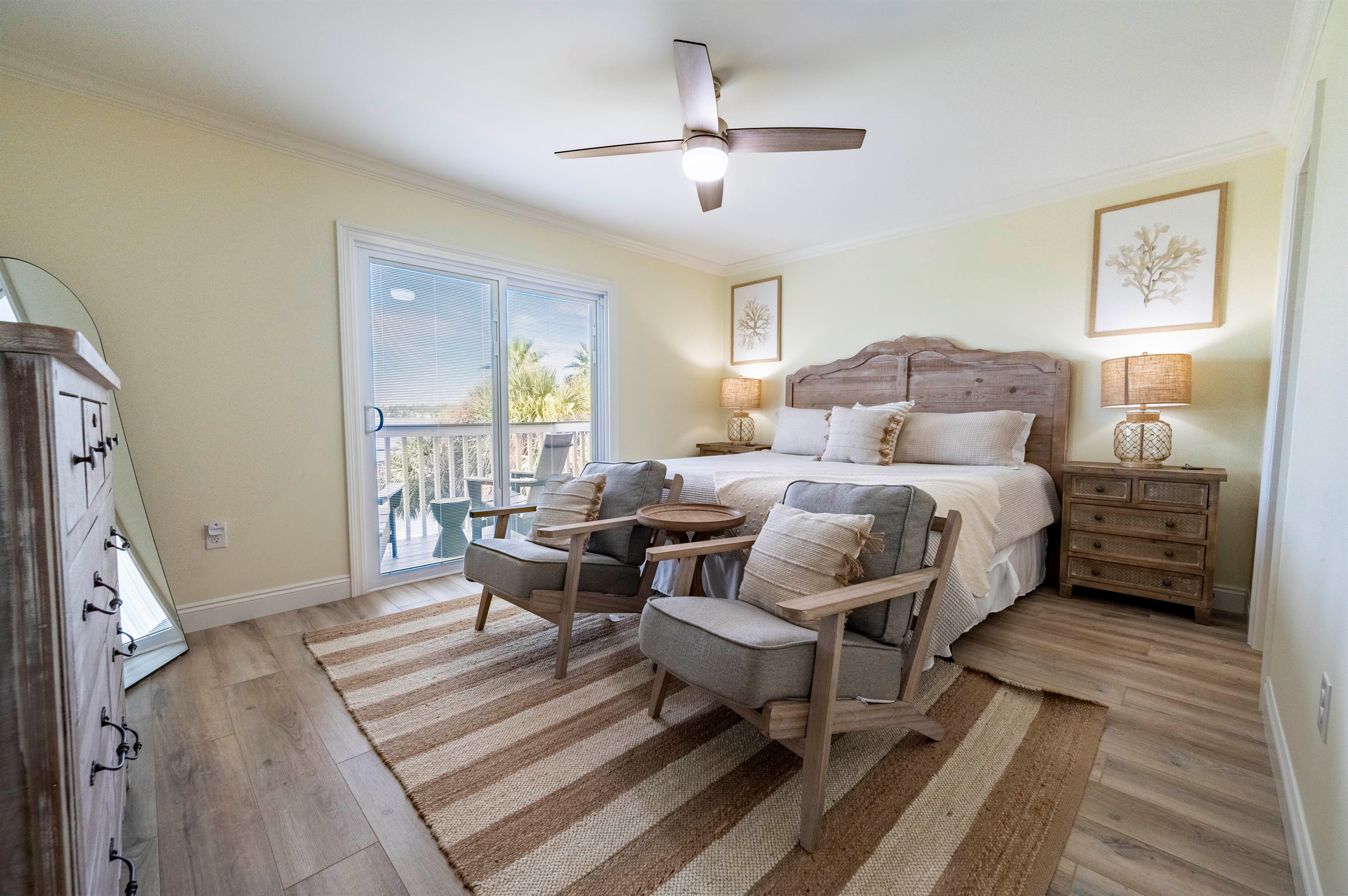 Spacious upstairs master suite with a king bed, warm wood furnishings, and soft neutral tones. Opens to a balcony overlooking Little Lagoon, with seating for quiet moments and fresh coastal air.