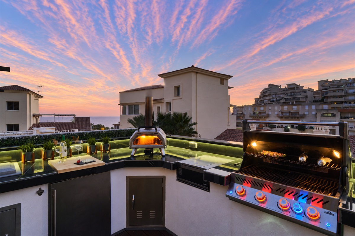 Fire up the built-in barbecue or the wood-fired pizza oven and enjoy cooking with a view. The fully equipped outdoor kitchen features a sink, fridge, and prep space with subtle lighting for evening meals. Dine under the open sky at the outdoor table, surro